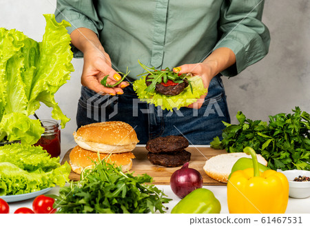 Woman is cooking tasty burger with cutlet, chesse and vegetables in the kitchen. 61467531