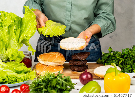 Girl puts a leaf of lettuce on the fried bread. Making a burger. Girl puts a leaf of lettuce on the fried bread. Making a burger. 61467717