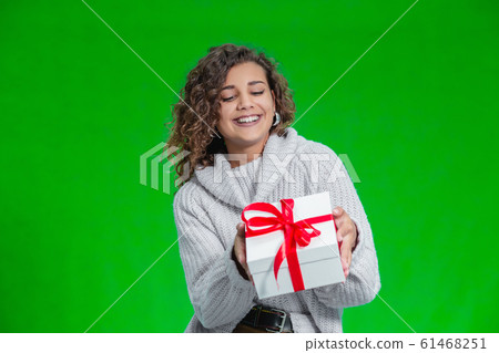 Christmas woman holding Christmas gifts in her arms wearing warm woolen sweater isolated on green background. 61468251