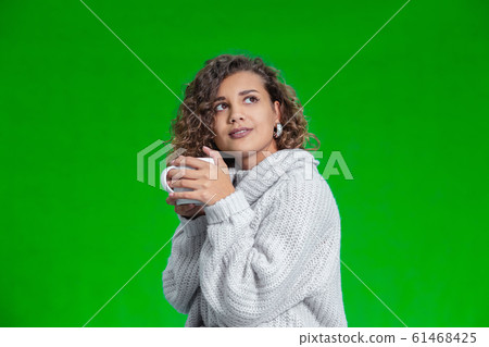 Young beautiful woman standing with cup of hot coffee wearing knitted warm sweater, dreaming about something inspiring. Young beautiful woman standing with cup of hot coffee wearing knitted warm sweater, dreaming about something inspiring. 61468425