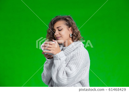 Sweet curly girl drinking hot cocoa standing against green background. Sweet curly girl drinking hot cocoa standing against green background. 61468429