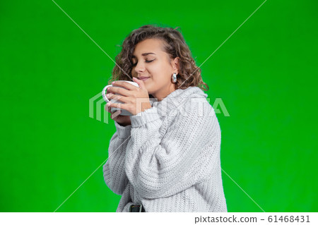 Closeup of a beautiful lady holding a cup of warm beverage, smelling aroma, looking completely pleased. Closeup of a beautiful lady holding a cup of warm beverage, smelling aroma, looking completely pleased. 61468431