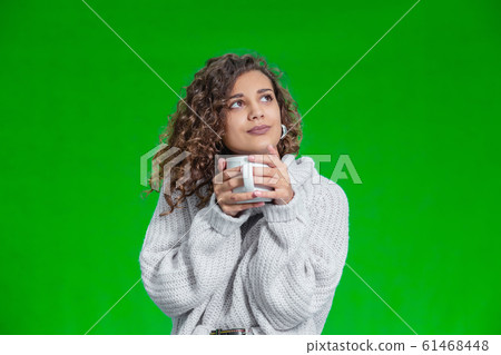 Young beautiful woman standing with cup of hot coffee wearing knitted warm sweater, dreaming about something inspiring. Young beautiful woman standing with cup of hot coffee wearing knitted warm sweater, dreaming about something inspiring. 61468448