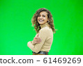 Happy young woman with a cute smile standing on green background with copy space. 61469269