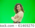Beautiful woman with kinky hair in beige clothes, isolated on green, looking pleased. 61469270