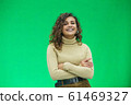 Beautiful woman with kinky hair in beige clothes, isolated on green, looking pleased. 61469327