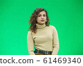 Beautiful woman with kinky hair in beige clothes, isolated on green, looking pleased. 61469340