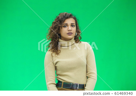 Beautiful woman with kinky hair in beige clothes, isolated on green, looking pleased. Beautiful woman with kinky hair in beige clothes, isolated on green, looking pleased. 61469340