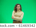 Portrait of a beautiful friendly african american woman with curly hairstyle and lovely smile isolated on a green background, her hands folded. 61469342