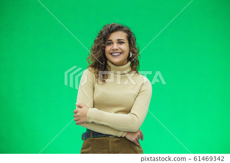 Portrait of a beautiful friendly african american woman with curly hairstyle and lovely smile isolated on a green background, her hands folded. Portrait of a beautiful friendly african american woman with curly hairstyle and lovely smile isolated on a green background, her hands folded. 61469342