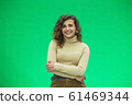 Portrait of a beautiful friendly african american woman with curly hairstyle and lovely smile isolated on a green background, her hands folded. 61469344