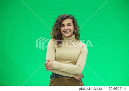 Portrait of a beautiful friendly african american woman with curly hairstyle and lovely smile isolated on a green background, her hands folded. 61469344