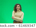 Portrait of a beautiful friendly african american woman with curly hairstyle and lovely smile isolated on a green background, her hands folded. 61469347