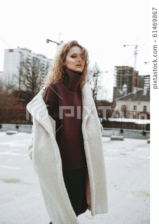 A girl with red curly hair in white coat poses on outdoor parking in cold autumn A girl with red curly hair in white coat poses on outdoor parking in cold autumn 61469867