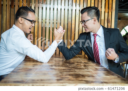 Two businessman expressed a serious expression and fighting by used arm wrestling on wood table. concept of business competition Two businessman expressed a serious expression and fighting by used arm wrestling on wood table. concept of business competition 61471206