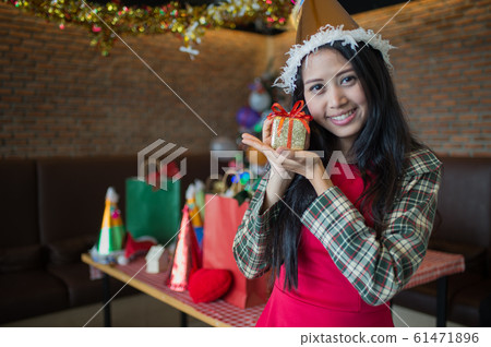 beautiful woman wear red dress and santa claus hat showing golden gift box on hand in restaurant. concept of Christmas party and New year party with copy space for text. beautiful woman wear red dress and santa claus hat showing golden gift box on hand in restaurant. concept of Christmas party and New year party with copy space for text. 61471896