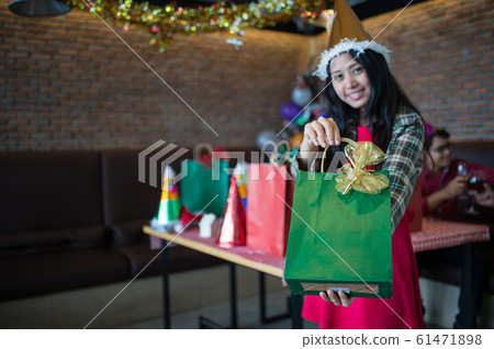 beautiful woman wear red dress and santa claus hat showing green gift bag on hand in restaurant. concept of Christmas party and New year party with copy space for text. beautiful woman wear red dress and santa claus hat showing green gift bag on hand in restaurant. concept of Christmas party and New year party with copy space for text. 61471898