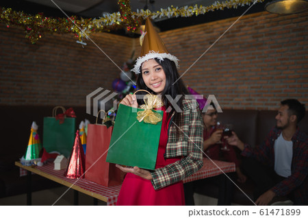 beautiful woman wear red dress and santa claus hat showing green gift bag on hand in restaurant. concept of Christmas party and New year party. beautiful woman wear red dress and santa claus hat showing green gift bag on hand in restaurant. concept of Christmas party and New year party. 61471899