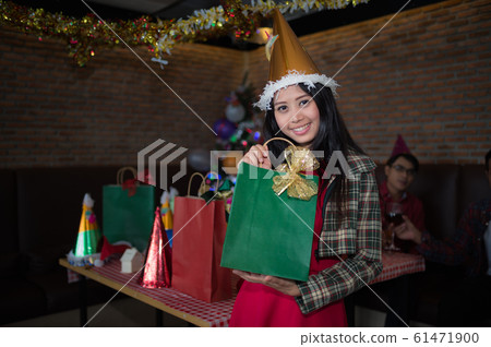 beautiful woman wear red dress and santa claus hat showing green gift bag on hand in restaurant. concept of Christmas party and New year party. beautiful woman wear red dress and santa claus hat showing green gift bag on hand in restaurant. concept of Christmas party and New year party. 61471900