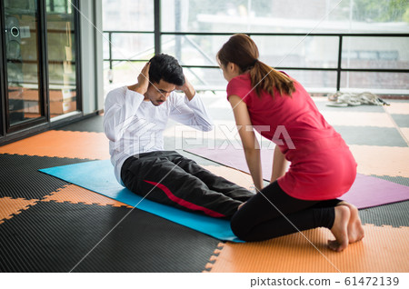 sportsman sit ups in gym with woman trainer in gym 61472139