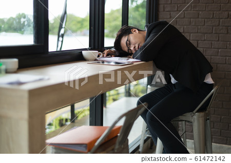 Tired businessman sleeping on counter bar at coffee shop with document, laptop and cup of coffee. 61472142