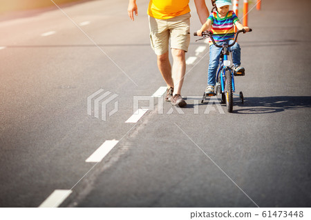 a child on a bicycle in helmet with father on asphalt road a child on a bicycle in helmet with father on asphalt road 61473448