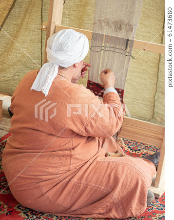 Times and Epochs Festival. Female Weaver Weaves a Canvas With a Pattern of Wool Yarn. Woman Weaves Using a Traditional Wooden Loom 61473680