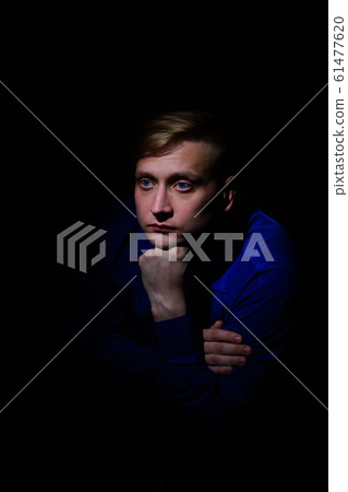portrait of a handsome young man in a sad shirt sits propping his beard with his hand on a black background portrait of a handsome young man in a sad shirt sits propping his beard with his hand on a black background 61477620
