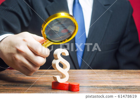 A man is studying a man who has come under repression by the huge Paragraph figurine. Suppression of protest moods. Usurpation of power. Deserved punishment of the criminal. Harassment and pressure 61478619
