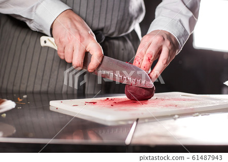 Closeup of hand with knife cutting fresh vegetable. Young chef cutting beet on a white cutting board closeup. Cooking in a restaurant kitchen 61487943