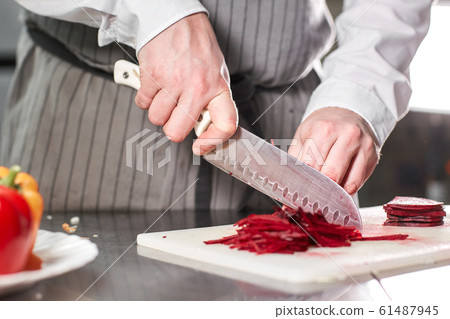 Closeup of hand with knife cutting fresh vegetable. Young chef cutting beet on a white cutting board closeup. Cooking in a restaurant kitchen 61487945