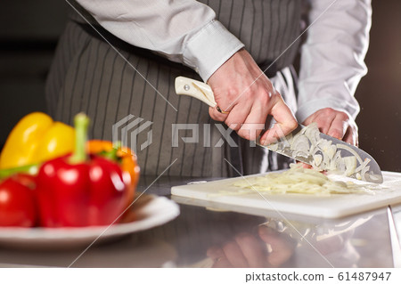 Closeup of hand with knife cutting fresh vegetable. Young chef cutting beet on a white cutting board closeup. Cooking in a restaurant kitchen 61487947
