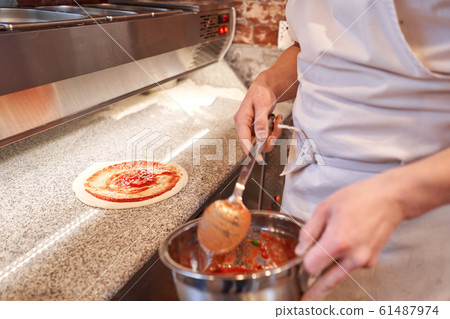 Cooking pizza. the workpiece poured tomato sauce. Closeup hand of chef. Baker in uniform and white apron cooking at kitchen Cooking pizza. the workpiece poured tomato sauce. Closeup hand of chef. Baker in uniform and white apron cooking at kitchen 61487974