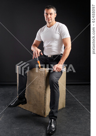 Athletic man with wrench on a black background. Not a typical worker, in a white t-shirt and trousers. 61488097
