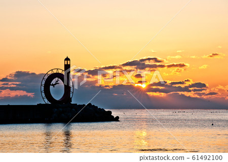 The sun rises through the clouds in the sea with a lighthouse The sun rises through the clouds in the sea with a lighthouse 61492100