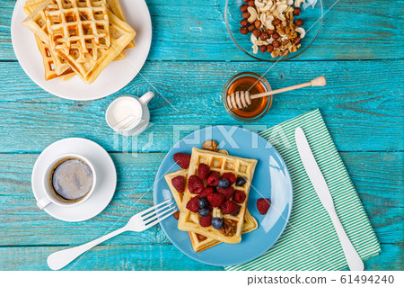 Homemade waffles with raspberries and blueberry, cup of coffee, milk and cutlery 61494240