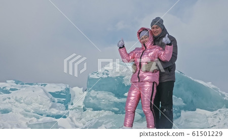 Couple has fun during winter walk against background of ice of frozen lake. Lovers lie on clear ice, have fun, kiss and hug. View from above. 61501229