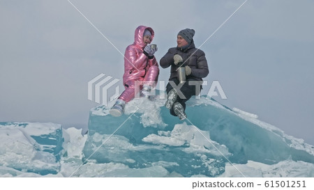 Couple has fun during winter walk against background of ice of frozen lake. Lovers lie on clear ice, have fun, kiss and hug. View from above. 61501251