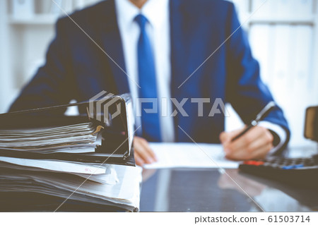 Binders with papers waiting to be processed with businessman or bookkeeper back in blur. Accounting planning budget. Audit, insurance and business concept Binders with papers waiting to be processed with businessman or bookkeeper back in blur. Accounting planning budget. Audit, insurance and business concept 61503714