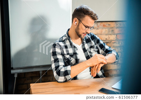 Young man checking the time in co-working space Young man checking the time in co-working space 61506377