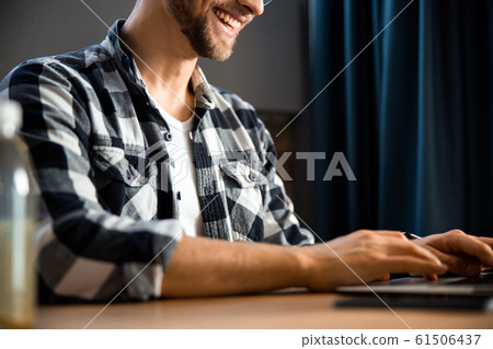 Happy young man sitting and typing on laptop 61506437