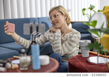 Smiling female blogger posing at camera while using smartphone Smiling female blogger posing at camera while using smartphone 61506935