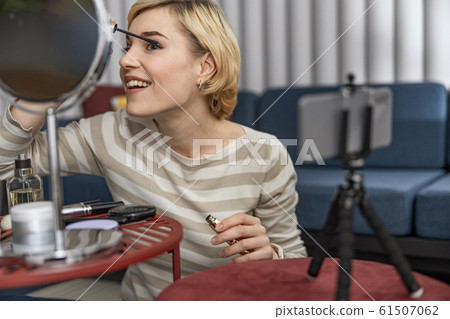 Happy young lady showing makeup on camera at home 61507062