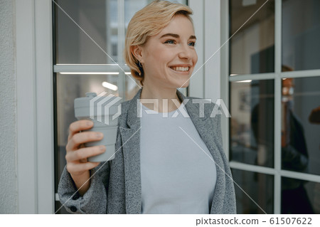 Happy young woman holding grey thermo cup 61507622