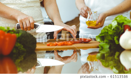 Closeup of human hands cooking in kitchen. Mother and daughter or two female friends cutting vegetables for fresh salad. Friendship, family dinner and lifestyle concepts Closeup of human hands cooking in kitchen. Mother and daughter or two female friends cutting vegetables for fresh salad. Friendship, family dinner and lifestyle concepts 61513586