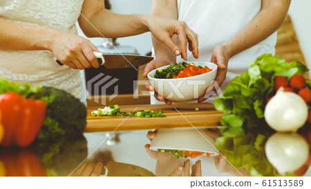 Closeup of human hands cooking in kitchen. Mother and daughter or two female friends cutting vegetables for fresh salad. Friendship, family dinner and lifestyle concepts Closeup of human hands cooking in kitchen. Mother and daughter or two female friends cutting vegetables for fresh salad. Friendship, family dinner and lifestyle concepts 61513589