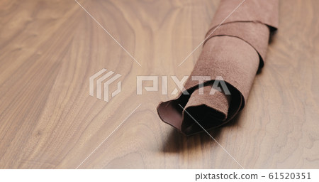 roll of brown leather piece on walnut table closeup 61520351