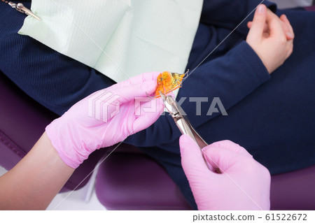 The dentist adjusts the anatomical orthodontic plate of orange acrylic and metal in the form of a jaw with a special tool. Close-up 61522672