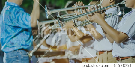 Male student with friends blow the trumpet with the band for performance on stage at night. Male student with friends blow the trumpet with the band for performance on stage at night. 61528751