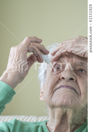 a senior woman applying eyedrops into her eyes a senior woman applying eyedrops into her eyes 61531929